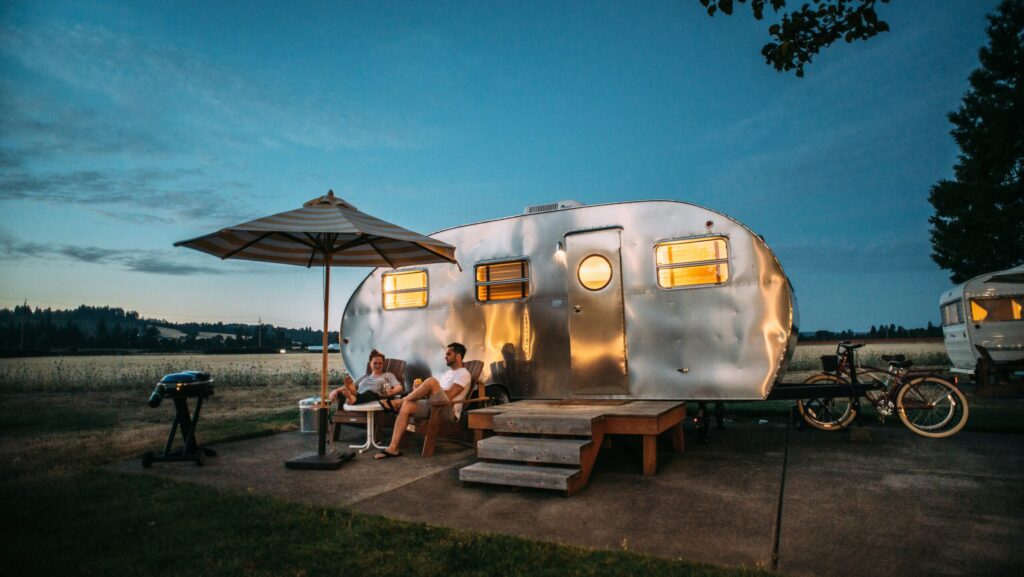 A couple sitting in chairs outside of their caravan enjoying the great outdoors at dusk.