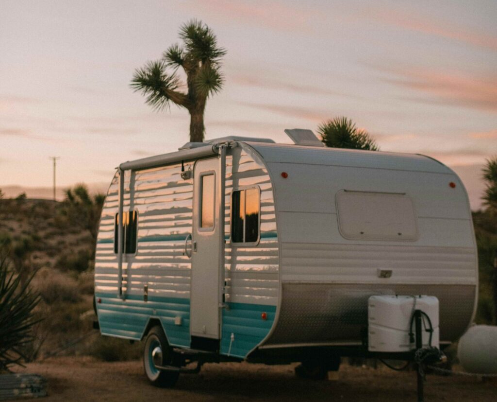 A classic white and blue RV caravan parked peacefully on a green grass field under a bright sky. Contact the NRCR team today to book your expert caravan service and repairs, ensuring your travels are always this relaxing.