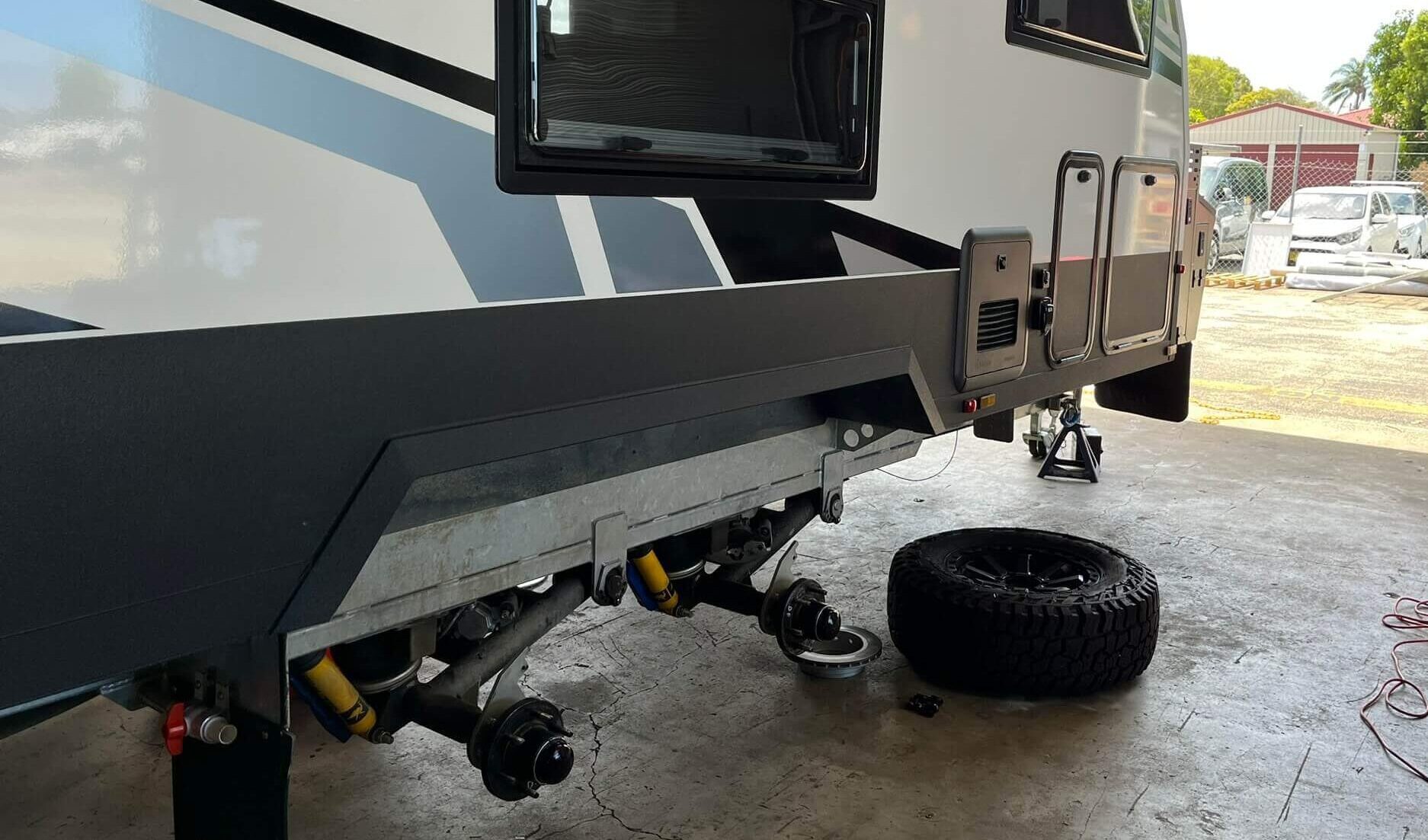 A modern caravan securely raised in our workshop for expert caravan service and repairs. The wheels are removed to perform detailed undercarriage and brake maintenance as part of our comprehensive caravan servicing.