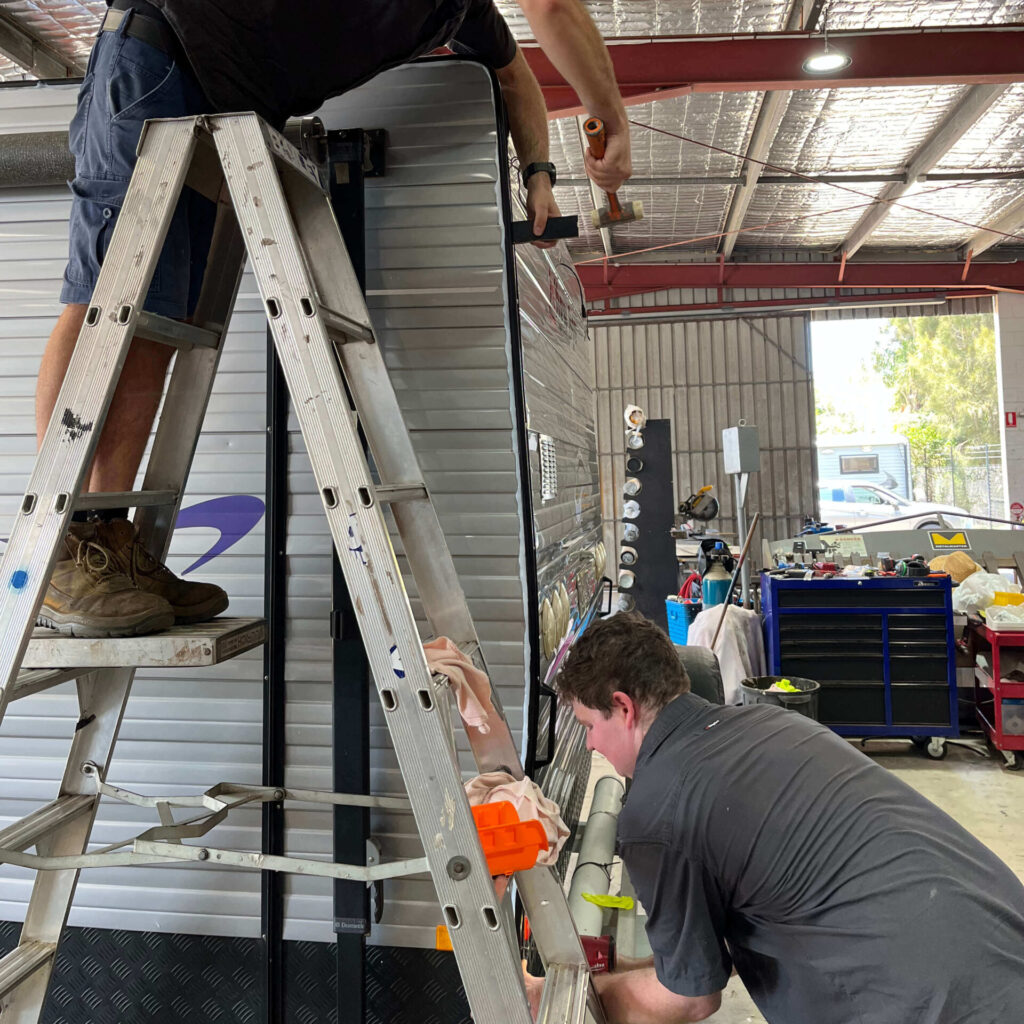Two expert Northern Rivers Caravan Repairs technicians performing detailed bodywork and internal repairs on a silver caravan inside our fully-equipped service workshop.