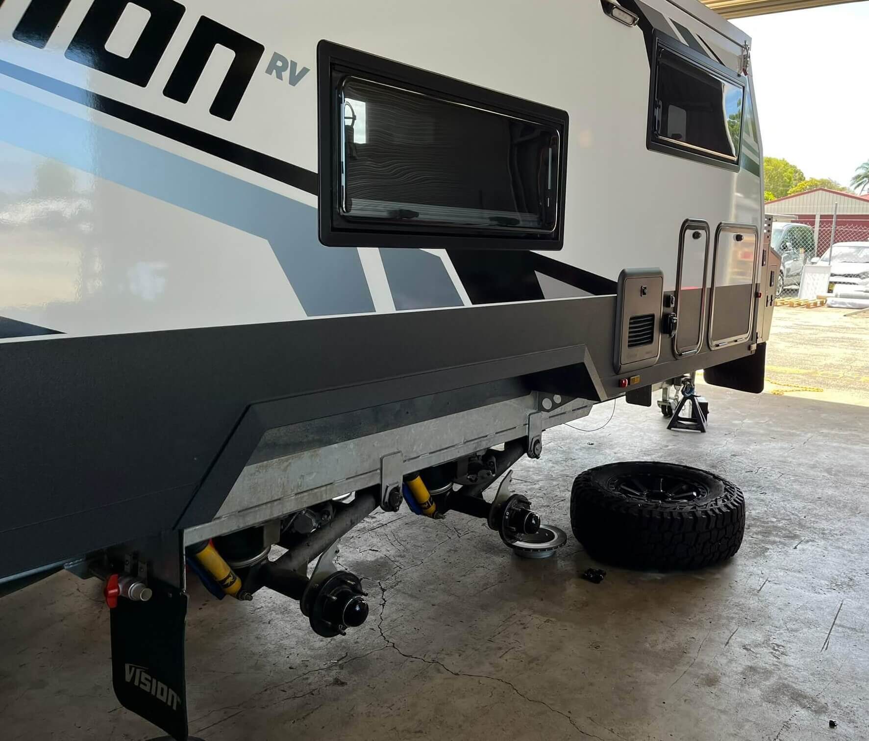 A modern caravan securely raised in our workshop for expert caravan service and repairs. The wheels are removed to perform detailed undercarriage and brake maintenance as part of our comprehensive caravan servicing.